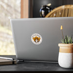 Round Byte & Bark Brew® sticker applied to silver laptop cover, partial desk props visible