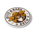 Round ceramic coaster displaying Byte & Bark Brew® logo with two golden retriever illustrations