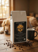 White Byte & Bark Brew® Colombia coffee bag with dog logo beside steaming mug and scattered beans
