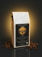 White bag of coffee with Byte & Bark Brew® dog logo and scattered beans on dark reflective surface