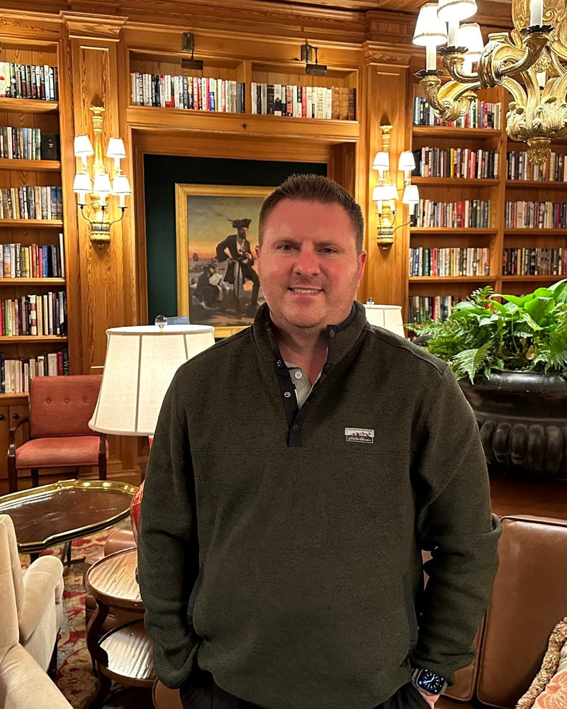 Man standing in a room with bookshelves, a painting, and decorative items.