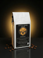 White bag of Byte & Bark Brew® Hazelnut whole bean coffee standing on black surface with scattered beans