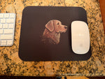 Black rectangular mouse pad with stylized dog profile print beside white Apple mouse and keyboard