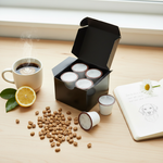Open black box of single-serve coffee pods on wooden table with steaming mug, scattered beans, lemon, notebook