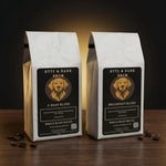 Two standing white coffee bags labeled Byte & Bark Brew® on a wooden surface with scattered coffee beans