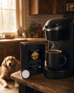 Steaming black mug beside Byte & Bark Brew® coffee pod box, single pod on rustic wooden table